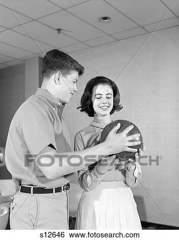 1960S Teenage Couple Bowling Alley Boy Helping Girl To Hold Ball Instruction Game Date Retro Vintage View Large Photo Image Stock Photograph - 1960S Teenage Couple Bowling Alley Boy Helping Girl To Hold Ball Instruction Game Date Retro Vintage. Fotosearch