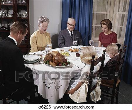 Stock Photograph - 1960S Three Generation Family Together Around Holiday Dinner Table Saying Grace Prayer Man Woman Boy Girl. Fotosearch