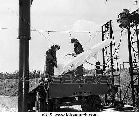 Stock Photography - 1960S U. S. Army Nike Guided Missle On Launch Pad Being Fueled Fuel By 2 Men In Fire Resistant Clothing . Fotosearch
