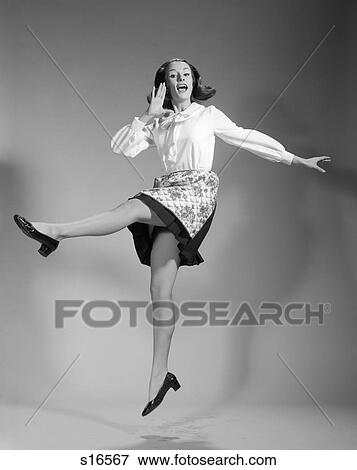 Stock Photo - 1960S Woman In Skirt & Apron Leaping In Air With Legs Apart & Hand To Mouth Calling Out . Fotosearch