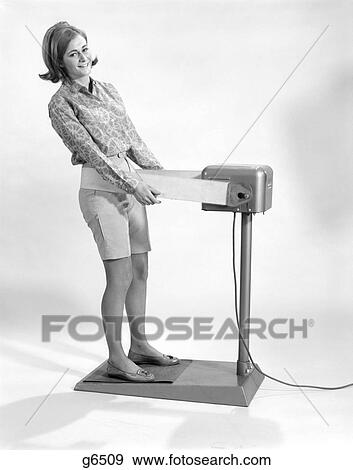 1960S Woman Standing On Exercise Machine Weight Fat Reducing Belt Shake Vibrate Wearing Print Shirt Bermuda Shorts View Large Photo Image Stock Photo - 1960S Woman Standing On Exercise Machine Weight Fat Reducing Belt Shake Vibrate Wearing Print Shirt Bermuda Shorts . Fotosearch