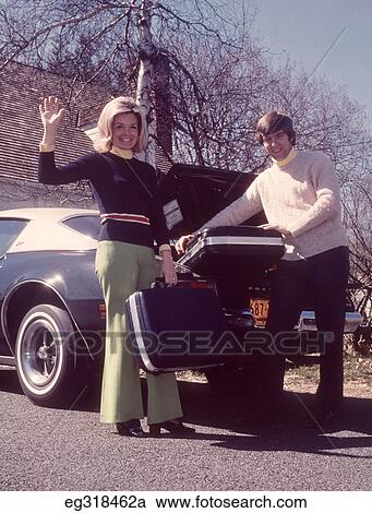 Stock Image - 1960S Woman Waving Man Loading Suitcases Into Car. Fotosearch