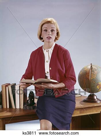 Stock Image - 1960S Woman With Open Book Sitting On Desk Between Books And Globe Teacher School Profession Speaker Job. Fotosearch