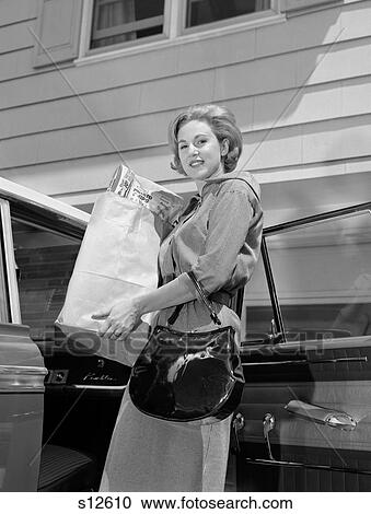 Stock Image - 1960S Woman With Patent Leather Handbag Unloading Grocery Bag From Car . Fotosearch
