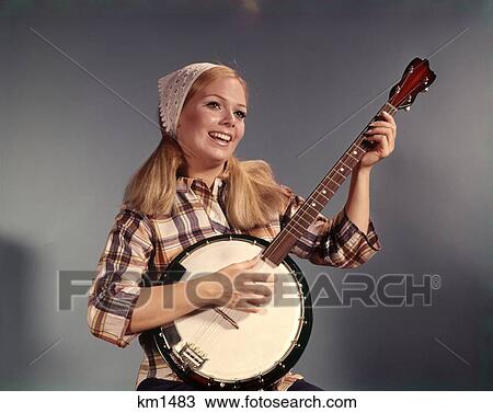 Stock Image - 1970 1970S 1960 1960S Young Blonde Woman Playing Banjo Triangle Scarf Plaid Shirt . Fotosearch