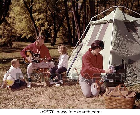 Parents With Son And Daughter Outside Tent Playing Guitar And Cooking On Grill Four Man Woman Boy Girl Vacation 1960S View Large Photo Image Stock Image - Parents With Son And Daughter Outside Tent Playing Guitar And Cooking On Grill Four Man Woman Boy Girl Vacation 1960S . Fotosearch