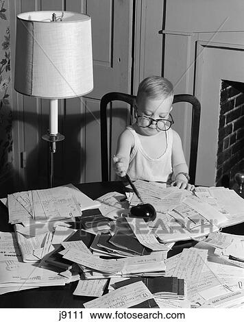 Stock Image - Young Boy At Desk Wearing Glasses And Undershirt Examining Personal Financial Documents Receipts Tax Forms Audit Irs 1960S. Fotosearch