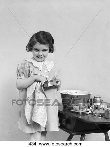 Picture - 1930s 1940s child girl drying toy dishes pots. Fotosearch