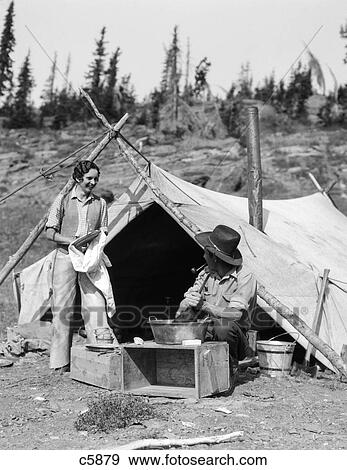 1930s couple woman at campsite by tarp tent washing drying dishes skillet man smoking pipe View Large Photo Image Stock Photo - 1930s couple woman at campsite by tarp tent washing drying dishes skillet man smoking pipe. Fotosearch