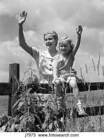 1930s girl sitting on fence with woman next to her in field waving View Large Photo Image Stock Image - 1930s girl sitting on fence with woman next to her in field waving. Fotosearch