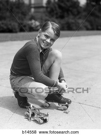 Stock Photo - 1930s smiling boy fastening on streamline metal roller skates. Fotosearch