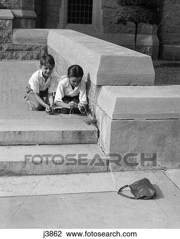 Stock Image - 1930s two boys playing trick with string tied to lost purse . Fotosearch