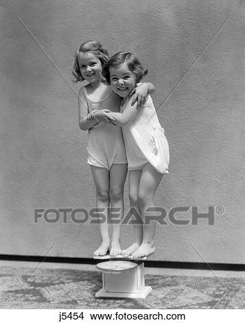1930s two little girls standing on scale arm in arm smiling View Large Photo Image Picture - 1930s two little girls standing on scale arm in arm smiling. Fotosearch