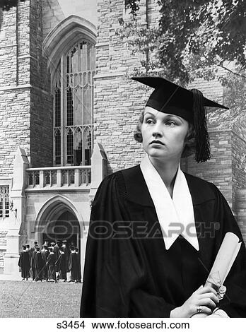 Picture - 1930s woman graduate cap gown holding a diploma standing in front stone building church school college university ceremony commencement graduation. Fotosearch