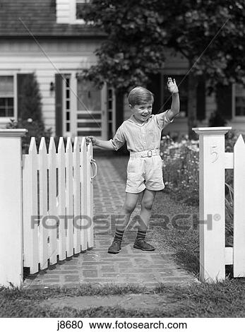 Stock Image - 1940s child standing near fence waving. Fotosearch