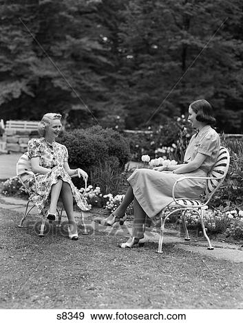 1940s two women sitting in lawn chairs talking smiling backyard garden both wearing cotton print dress and spectator shoes View Large Photo Image Stock Photo - 1940s two women sitting in lawn chairs talking smiling backyard garden both wearing cotton print dress and spectator shoes. Fotosearch