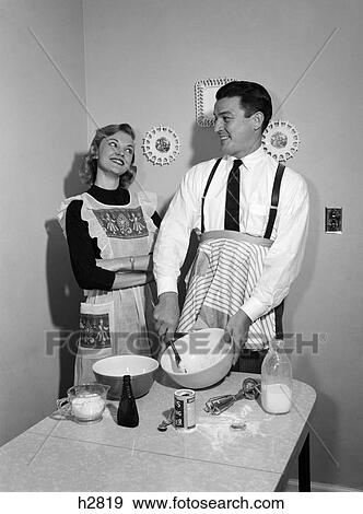 1950s couple husband wife kitchen table both wear apron man mixing spoon bowl blending ingredients woman arms folded smiling up at man satisfied amused View Large Photo Image Stock Photo - 1950s couple husband wife kitchen table both wear apron man mixing spoon bowl blending ingredients woman arms folded smiling up at man satisfied amused. Fotosearch