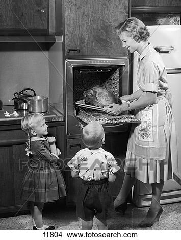 1950s daughter and son watching mother remove roast thanksgiving turkey dinner from electric kitchen oven View Large Photo Image Picture - 1950s daughter and son watching mother remove roast thanksgiving turkey dinner from electric kitchen oven. Fotosearch
