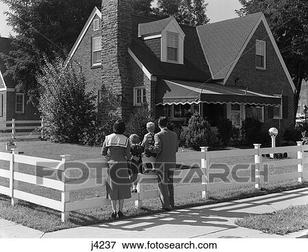 1950s family standing by white fence looking at brick house View Large Photo Image Stock Photo - 1950s family standing by white fence looking at brick house. Fotosearch