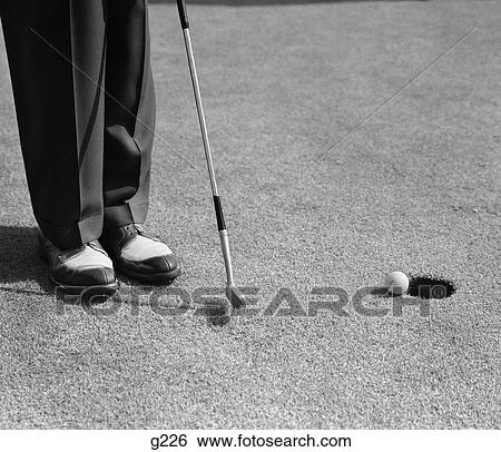 Stock Photograph - 1950s man knees down putt on golf green. Fotosearch