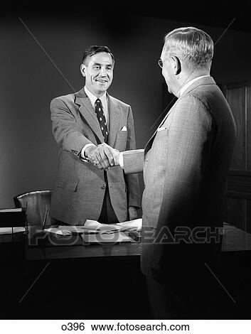 1950s men shaking hands suits desk business paper work View Large Photo Image Stock Photograph - 1950s men shaking hands suits desk business paper work. Fotosearch