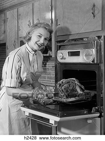 1950s smiling woman housewife wearing apron taking large roast beef from electric oven in kitchen looking at camera View Large Photo Image Stock Photo - 1950s smiling woman housewife wearing apron taking large roast beef from electric oven in kitchen looking at camera. Fotosearch