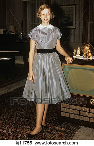 Stock Photography - 1950s teenage girl dressed for her first date in gray silky dress posed by television set. Fotosearch