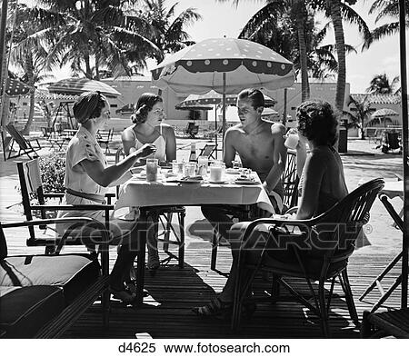 Stock Photography - 1950s three women and one man sitting at tropical pool side table talking. Fotosearch