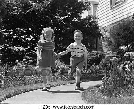 1950s two children holding hands smiling walking along sidewalk View Large Photo Image Stock Photography - 1950s two children holding hands smiling walking along sidewalk. Fotosearch