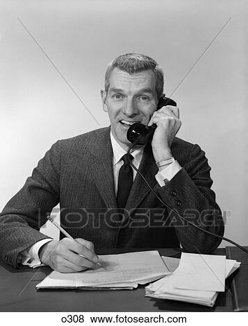 1960s 1950s business man phone desk paper work talking writing View Large Photo Image Stock Photo - 1960s 1950s business man phone desk paper work talking writing. Fotosearch