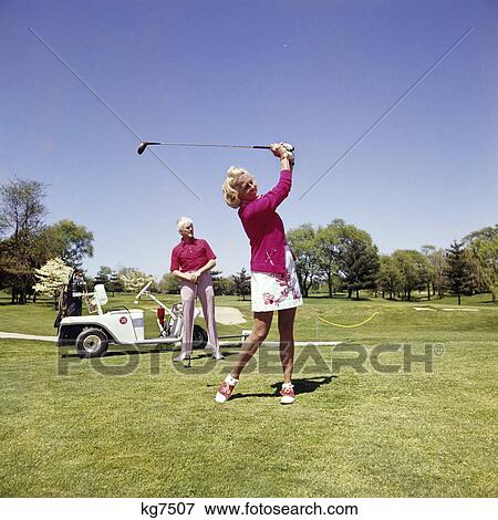 1960s 1970s mature woman swinging golf club as man stands by golf cart View Large Photo Image Stock Photo - 1960s 1970s mature woman swinging golf club as man stands by golf cart. Fotosearch