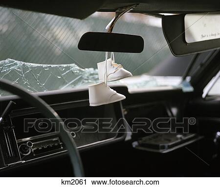 Stock Image - 1960s 1970s pair white baby shoes dangling from rear view mirror of wrecked car with shattered glass windshield. Fotosearch