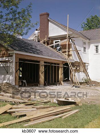Stock Photo - 1960s 1970s workers building two car garage addition onto suburban home. Fotosearch