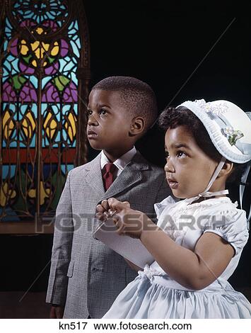 Stock Photo - 1960s african american boy and girl brother and sister standing by stained glass window in church. Fotosearch