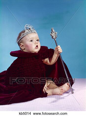 Picture - 1960s baby dressed as royal queen in a velvet robe cloak cape rhinestone tiara crown and scepter wand. Fotosearch