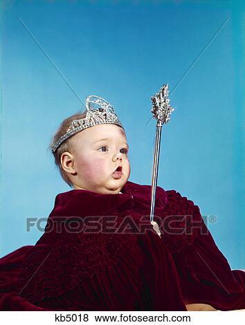 Stock Photo - 1960s baby dressed as royal queen in a velvet robe cloak cape rhinestone tiara crown and scepter wand. Fotosearch