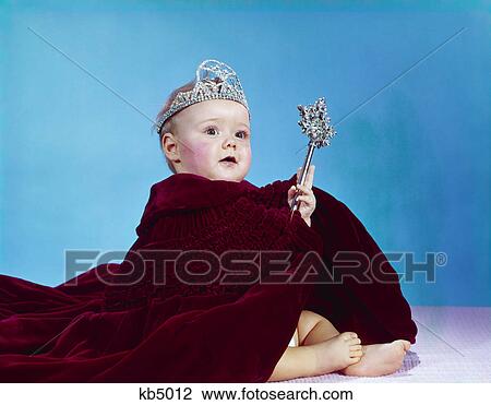 Stock Image - 1960s baby dressed as royal queen in velvet robe cloak cape rhinestone tiara crown and scepter wand. Fotosearch