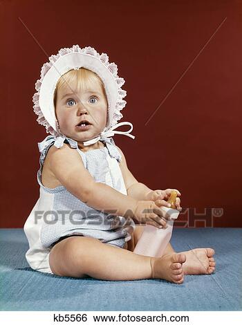 1960s baby girl ruffled bonnet holding bottle funny facial expression View Large Photo Image Stock Photograph - 1960s baby girl ruffled bonnet holding bottle funny facial expression. Fotosearch