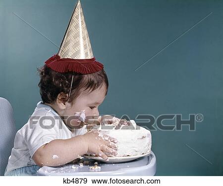 1960s baby in highchair wearing birthday hat eating whole birthday cake View Large Photo Image Stock Photo - 1960s baby in highchair wearing birthday hat eating whole birthday cake. Fotosearch