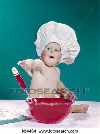 1960s baby wearing chef hat with red mixing bowl and spoon funny facial expression View Large Photo Image Picture - 1960s baby wearing chef hat with red mixing bowl and spoon funny facial expression. Fotosearch