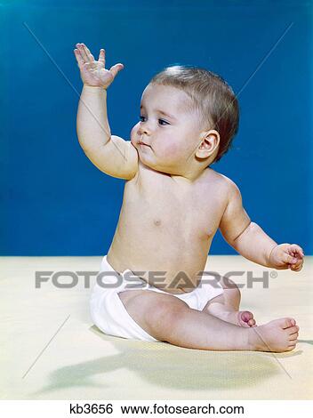 Stock Photograph - 1960s baby wearing cloth diaper looking over shoulder waving with raised arm gesture. Fotosearch