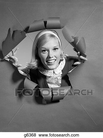 Stock Photo - 1960s blond woman breaking through ripped paper smiling wearing headband. Fotosearch