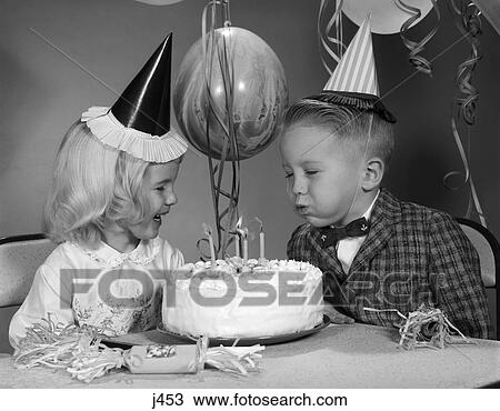 Stock Image - 1960s child blowing out candles on birthday cake party. Fotosearch