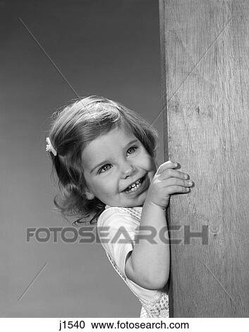 Stock Image - 1960s child smiling peering around corner. Fotosearch