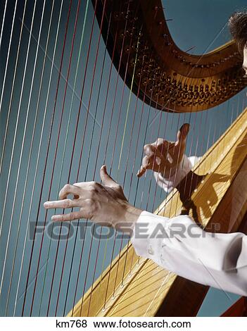 Stock Photo - 1960s close up of woman's hands playing harp plucking strings. Fotosearch