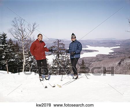 1960s couple man woman skiers standing top of hill with vista view winter lake View Large Photo Image Stock Photo - 1960s couple man woman skiers standing top of hill with vista view winter lake. Fotosearch