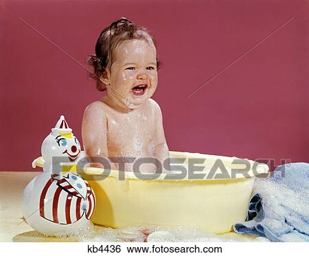 1960s crying brunette baby sitting in yellow plastic bath tub with toy clown View Large Photo Image Stock Photograph - 1960s crying brunette baby sitting in yellow plastic bath tub with toy clown. Fotosearch