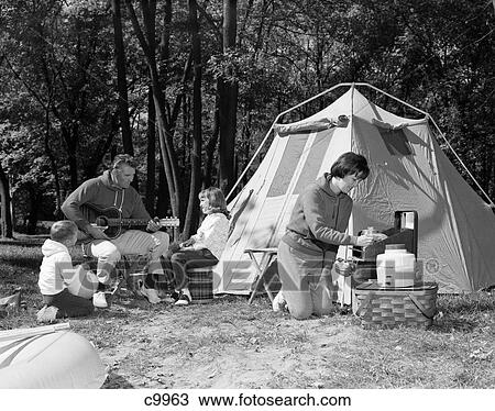 Stock Image - 1960s family camping tent mother cooking father playing guitar. Fotosearch