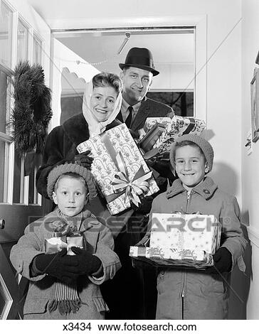 1960s family standing in doorway of home wearing winter coats & hats holding wrapped gifts View Large Photo Image Picture - 1960s family standing in doorway of home wearing winter coats & hats holding wrapped gifts. Fotosearch