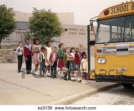 Stock Photo - 1960s group of elementary kids in line getting onto yellow school bus. Fotosearch